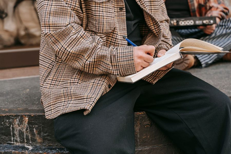 A person writing in a notebook while sitting outdoors
