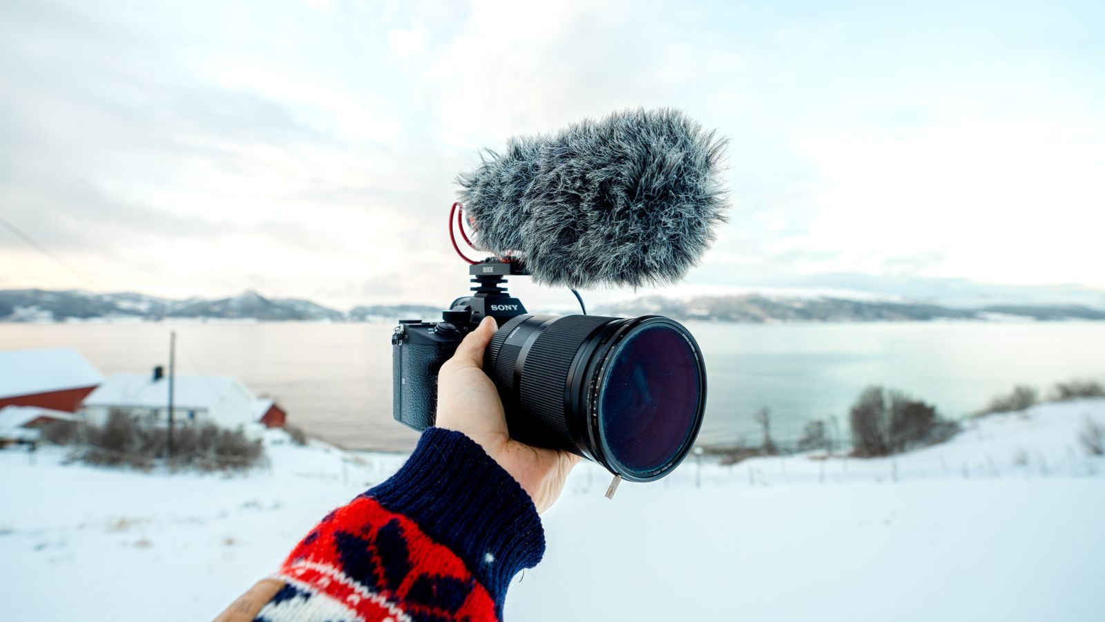 A camera with a microphone held up against a snowy coastline, as used for cruise reviews on YouTube